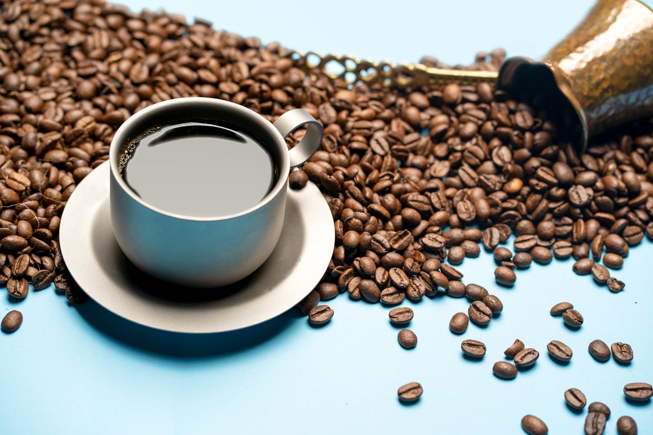A cup of black coffee with roasted beans on a light blue surface, evoking a fresh morning brew.