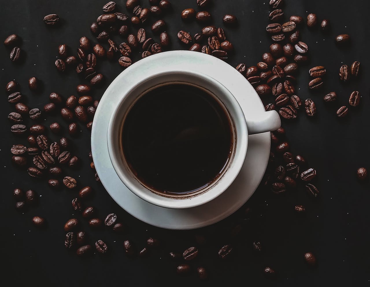 Aesthetic top view of black coffee in a white cup surrounded by coffee beans.