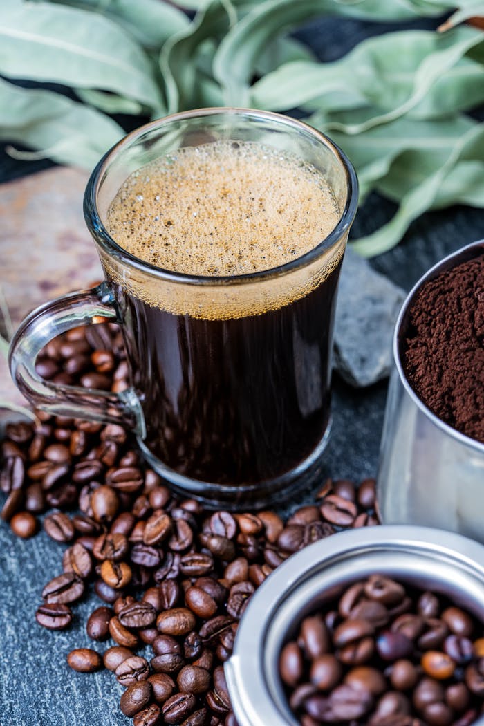A glass of freshly brewed coffee surrounded by coffee beans and ground coffee.