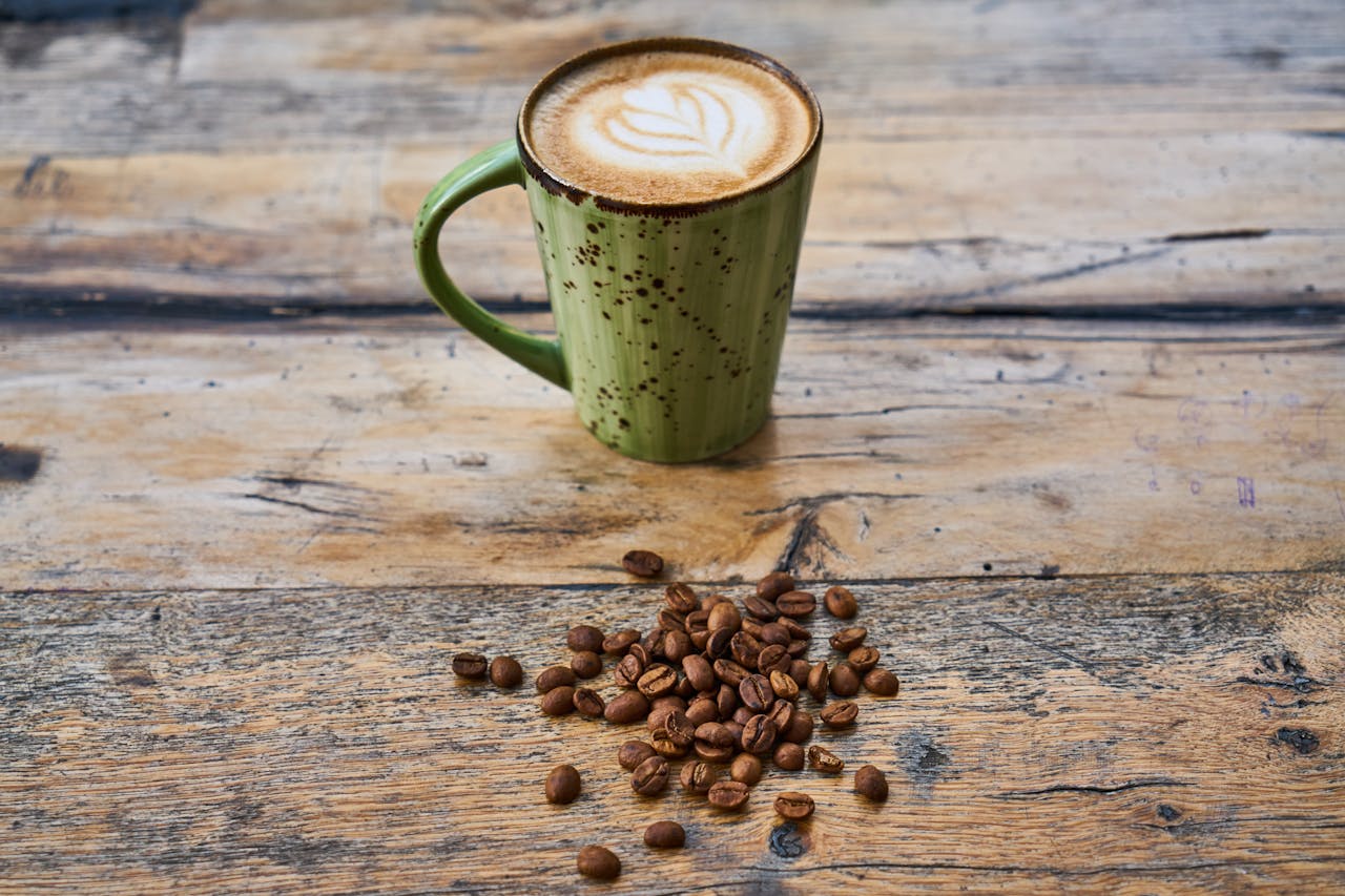 A green mug of cappuccino with coffee beans on a rustic wooden surface.