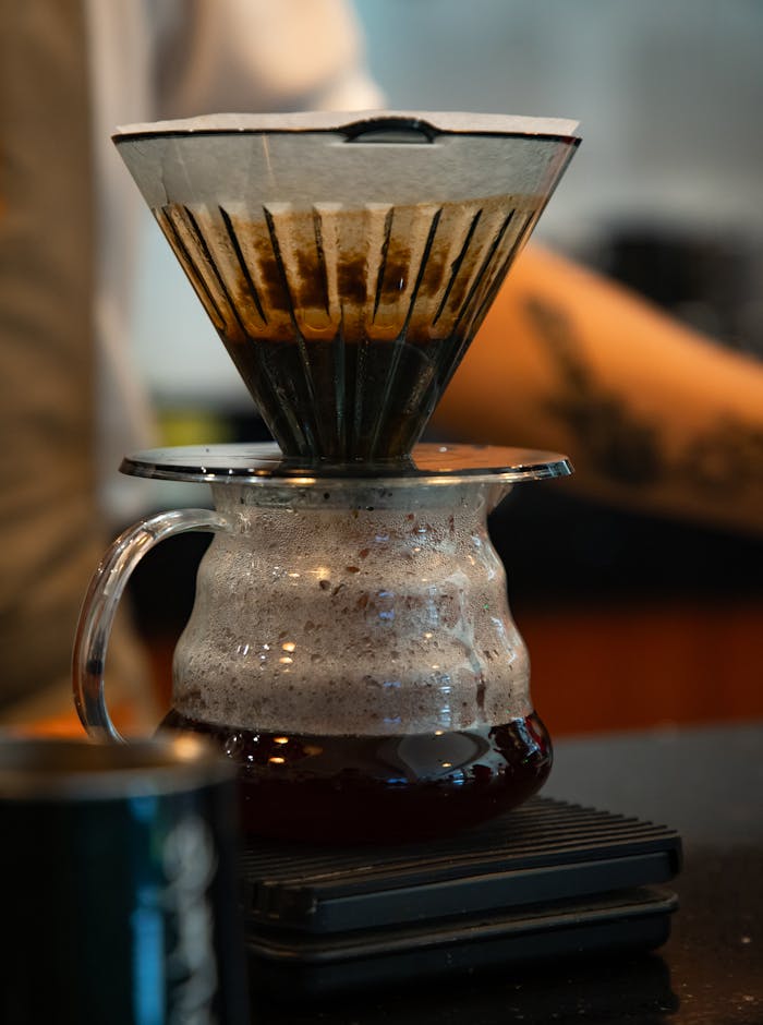 Close-up of coffee brewing in a glass pour-over device on a scale in a cozy café.