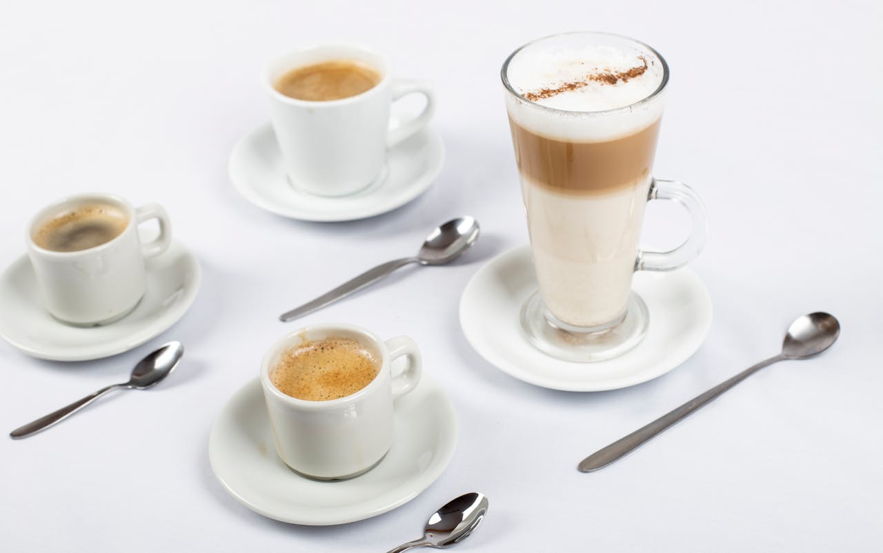 A stylish arrangement of coffee cups, saucers, and teaspoons on a white surface.